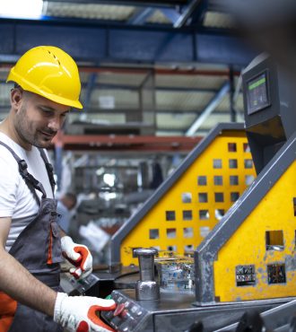 Portrait of factory worker working on industrial machine in production plant.